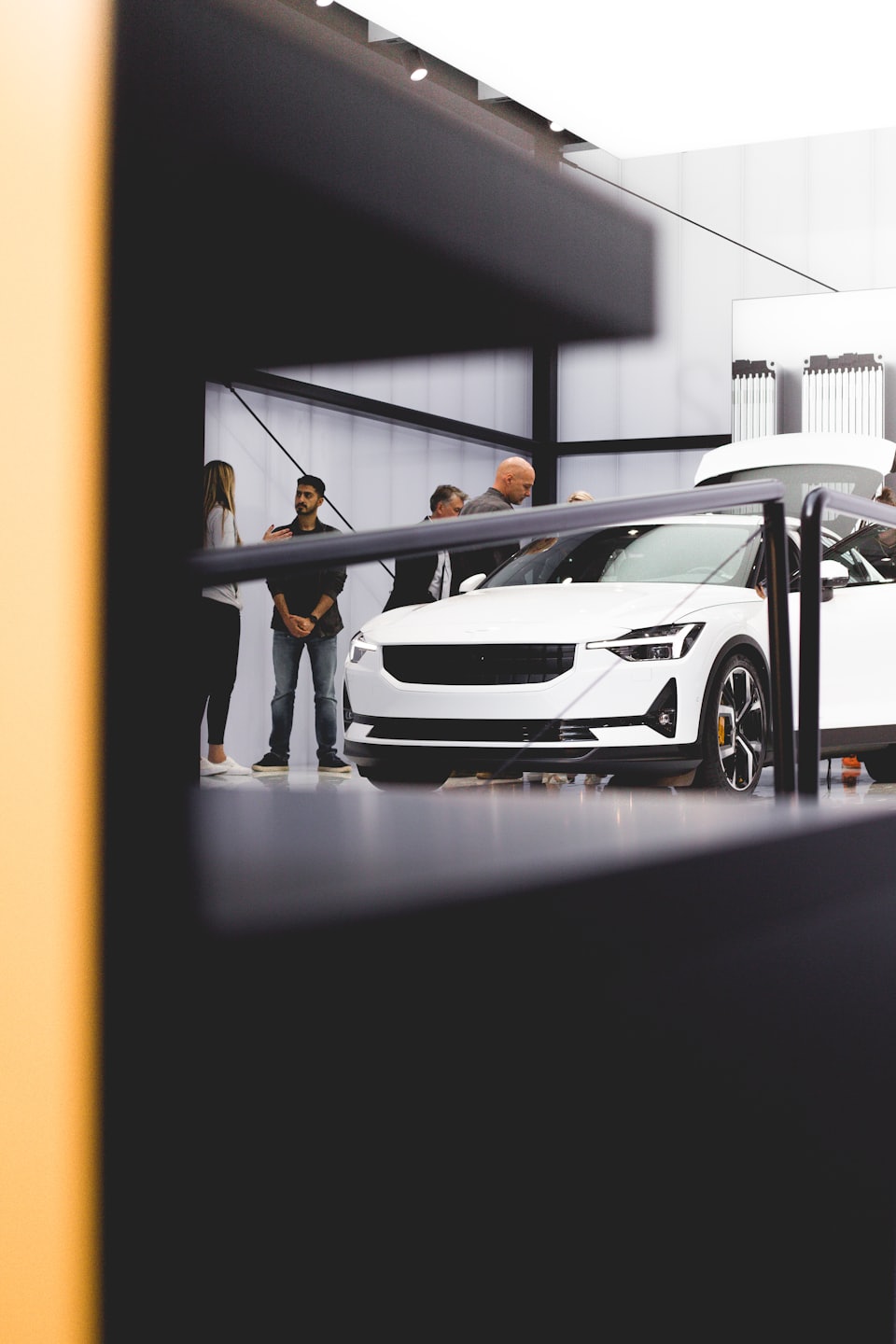 Menschen betrachten einen weißen Wagen in einer modernen Autohalle.